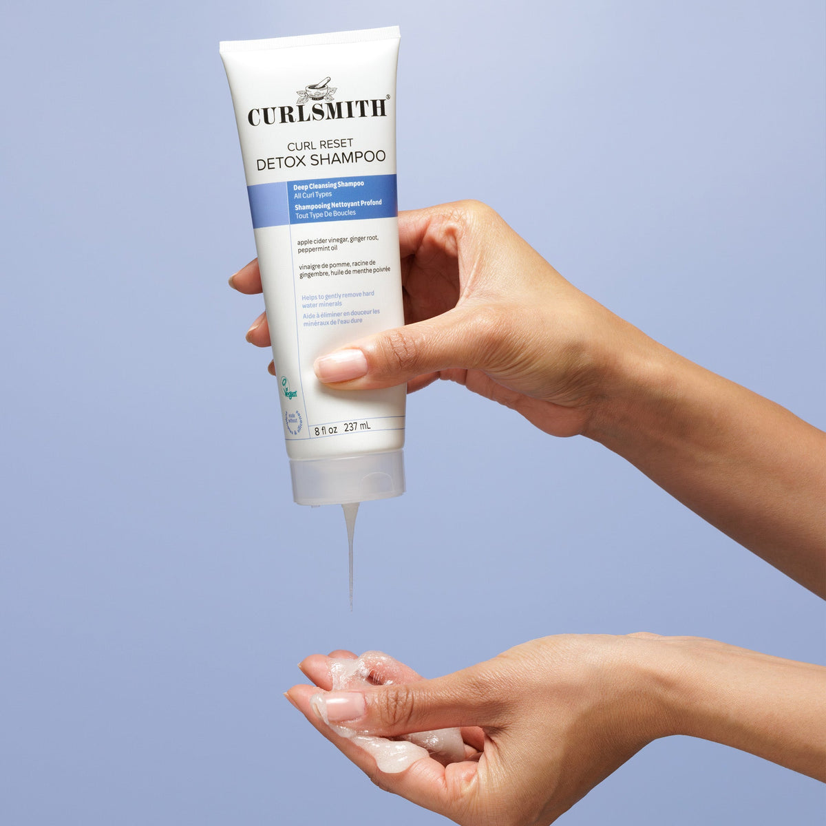 Curlsmith Curl Reset Detox Shampoo being dispensed into a hand against a light blue background