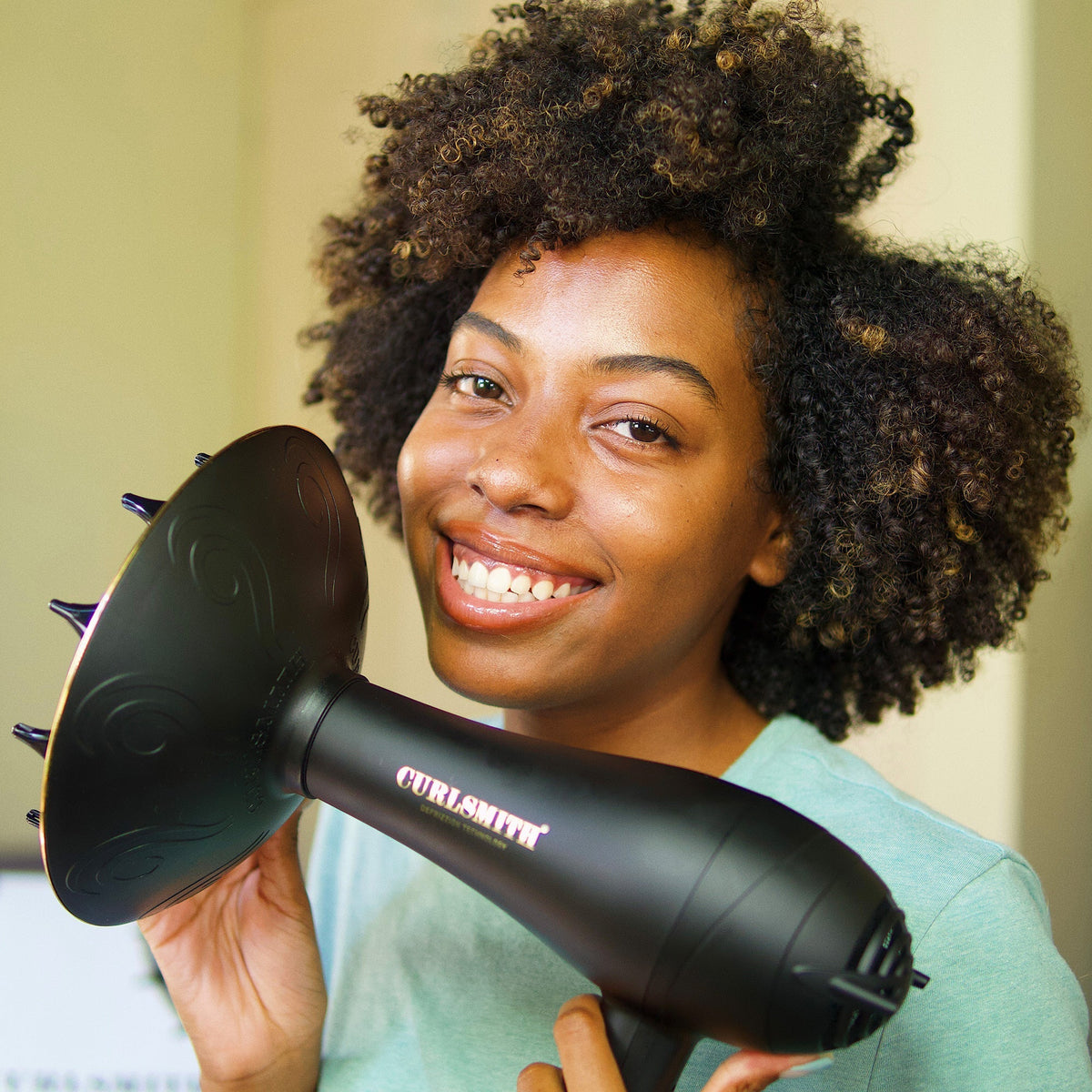 Woman holding a black hair dryer with spikes, smiling at the camera.