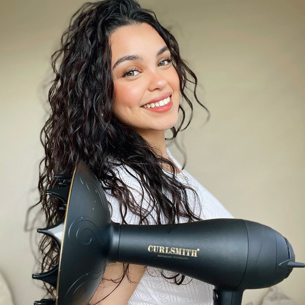 Woman using a Curlsmith hair dryer with curly hair, smiling.