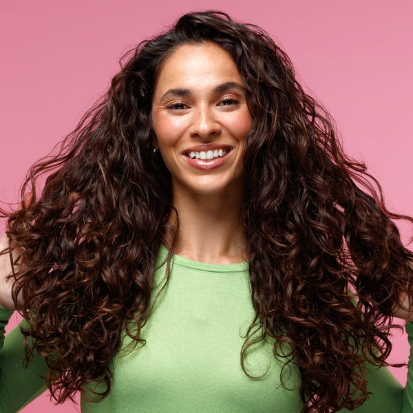 Curly Haired woman in front of pink background