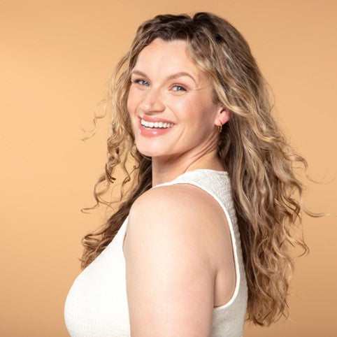 Woman with wavy hair smiling in front of a light orange background.