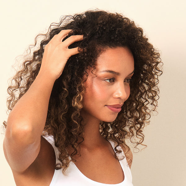 Woman with curly hair touching her hair against a beige background
