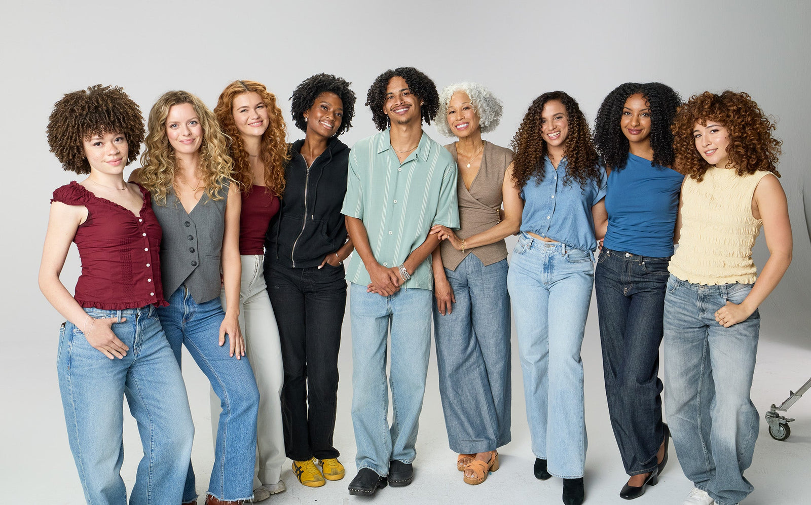 Group of women standing together wearing jeans on a plain background